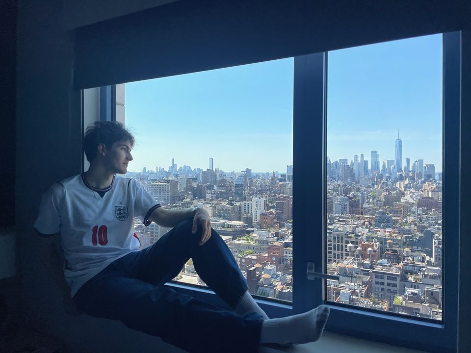 Matt sitting on a window ledge in an England number 10 shirt, looking out over the New York City skyline